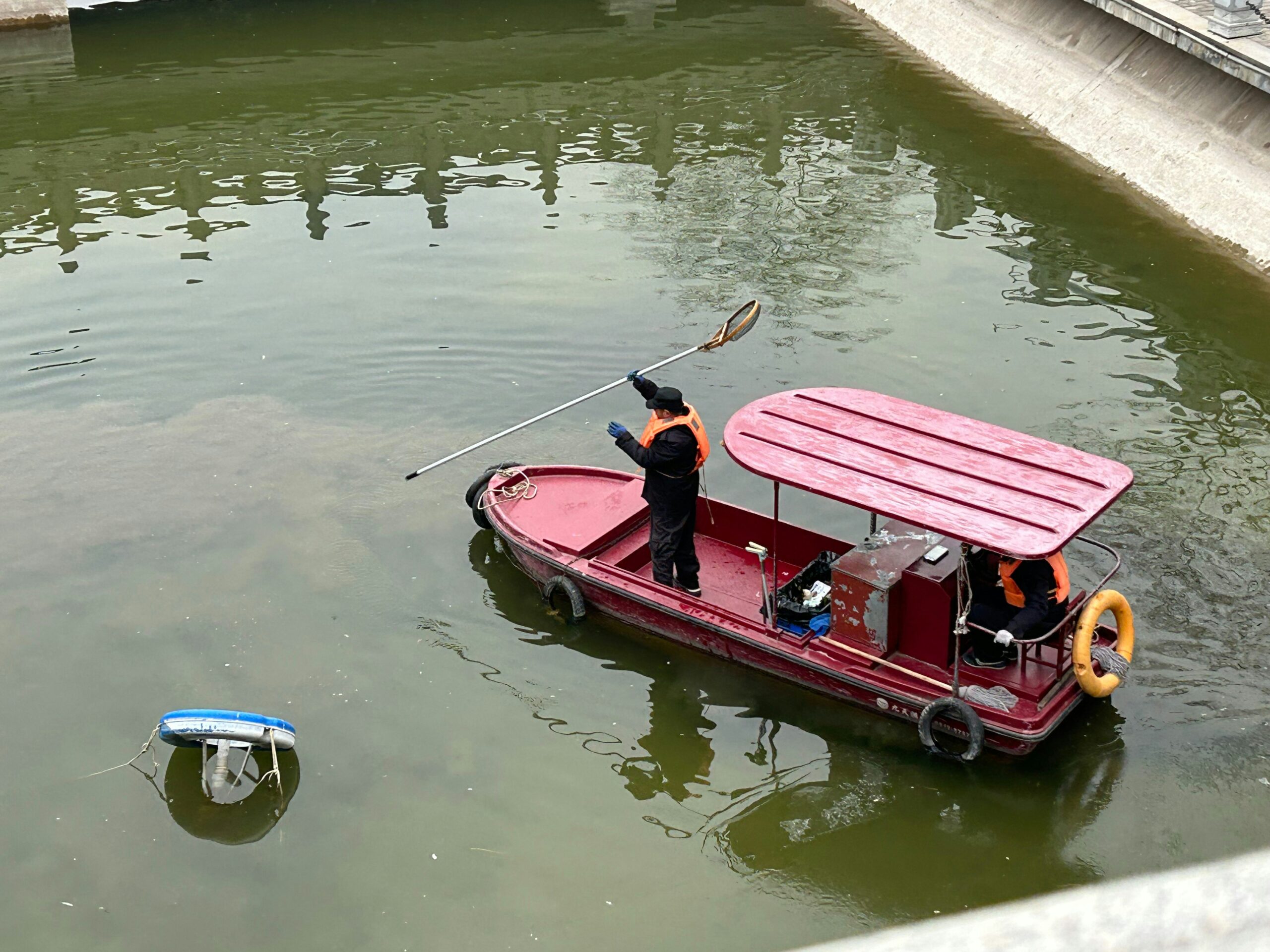 Some workers cleaning up floating debris from the water with an old boat manually and clearly not aware of RanMarine's WasteShark plus.