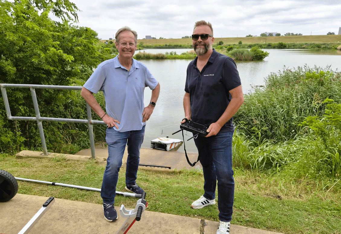 Mike Foss and Richard Hardiman in front of a lake with a WasteShark